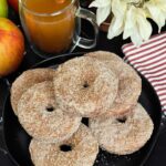 Baked apple cider donuts stacked on a dark plate on a dark surface.