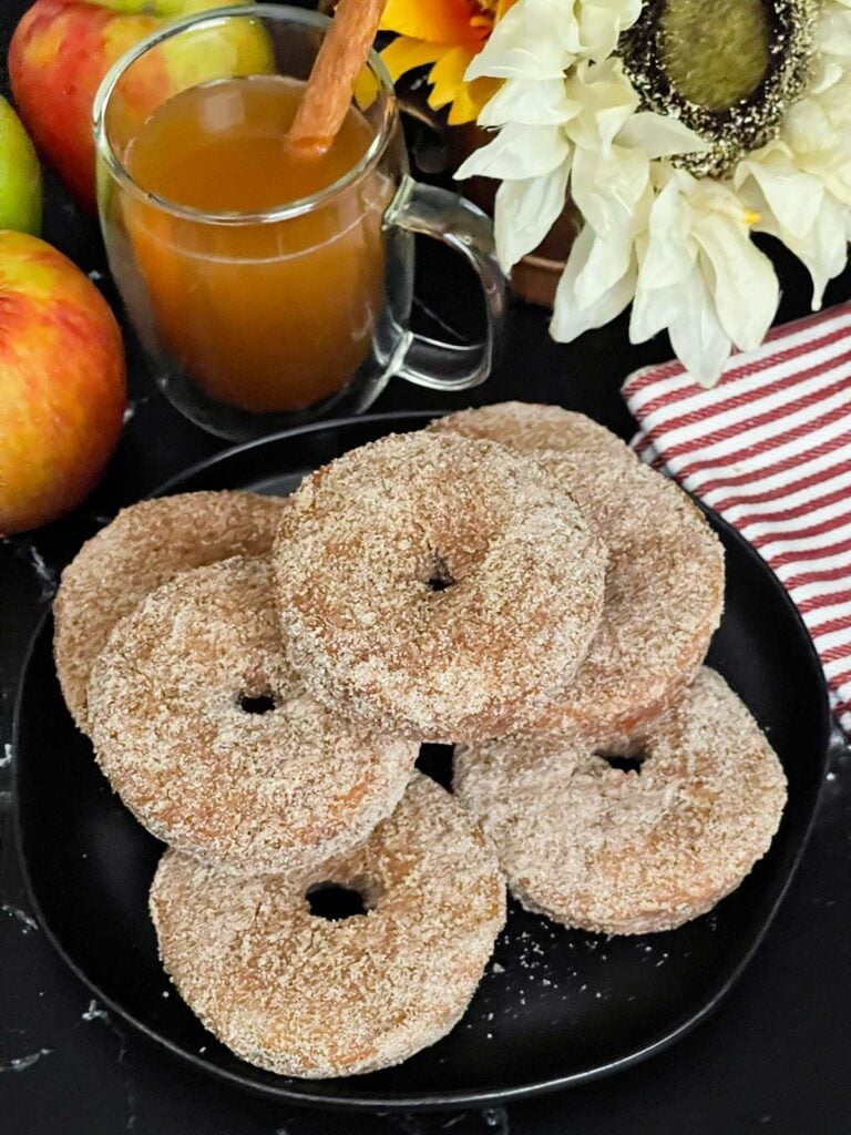Baked apple cider donuts stacked on a dark plate on a dark surface.