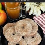Baked apple cider donuts stacked on a dark plate on a dark surface.
