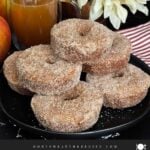 Baked apple cider donuts stacked on a dark plate on a dark surface.