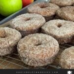 Baked apple cider donuts on a wire rack over a parchment paper lined baking pan.