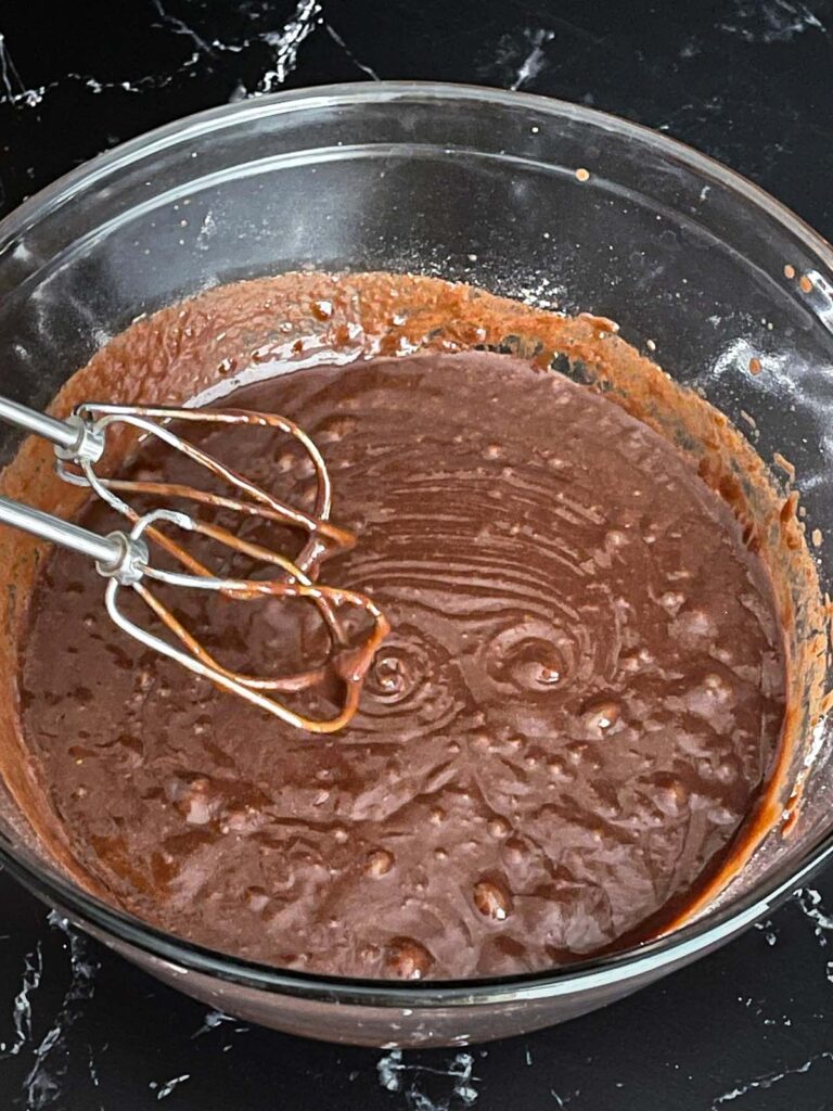 Buttermilk brownie batter mixed in a large glass bowl on a dark surface.