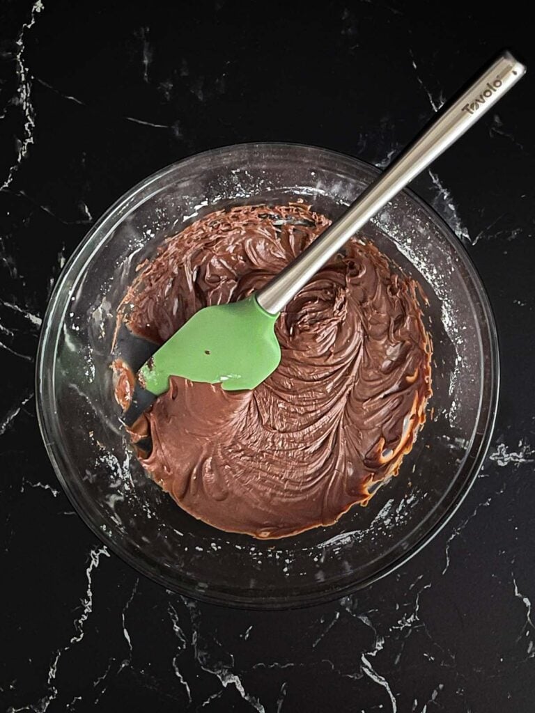 Buttermilk chocolate icing mixed in a large glass bowl on a dark surface.