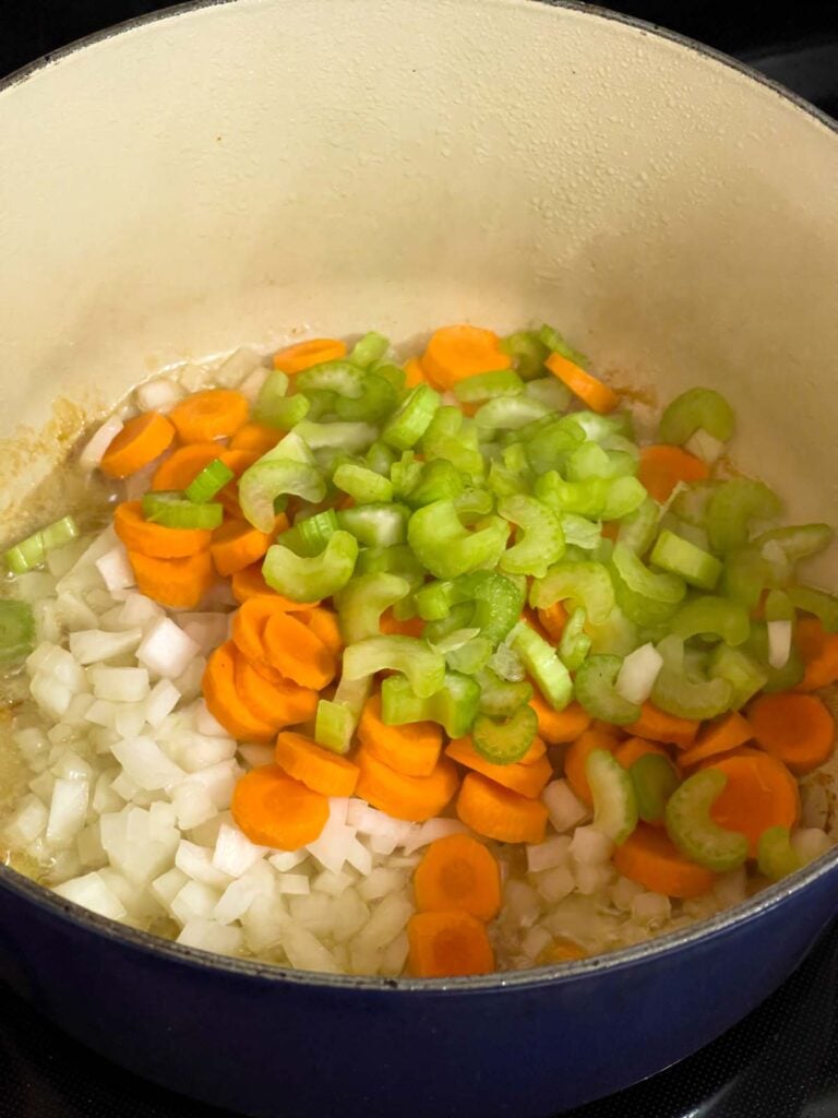 Onions, celery, and carrots sautéing in a large dutch oven for the chicken noodle soup recipe.