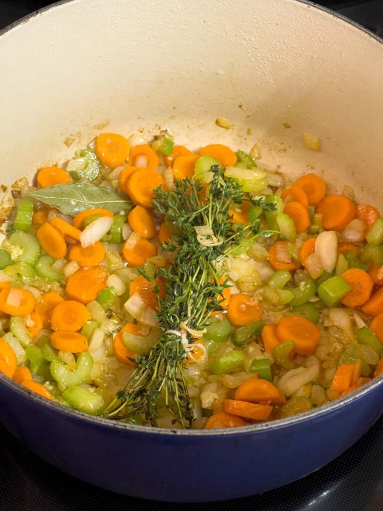 Garlic, fresh thyme, and a bay leaf added to the vegetables in a large dutch oven.