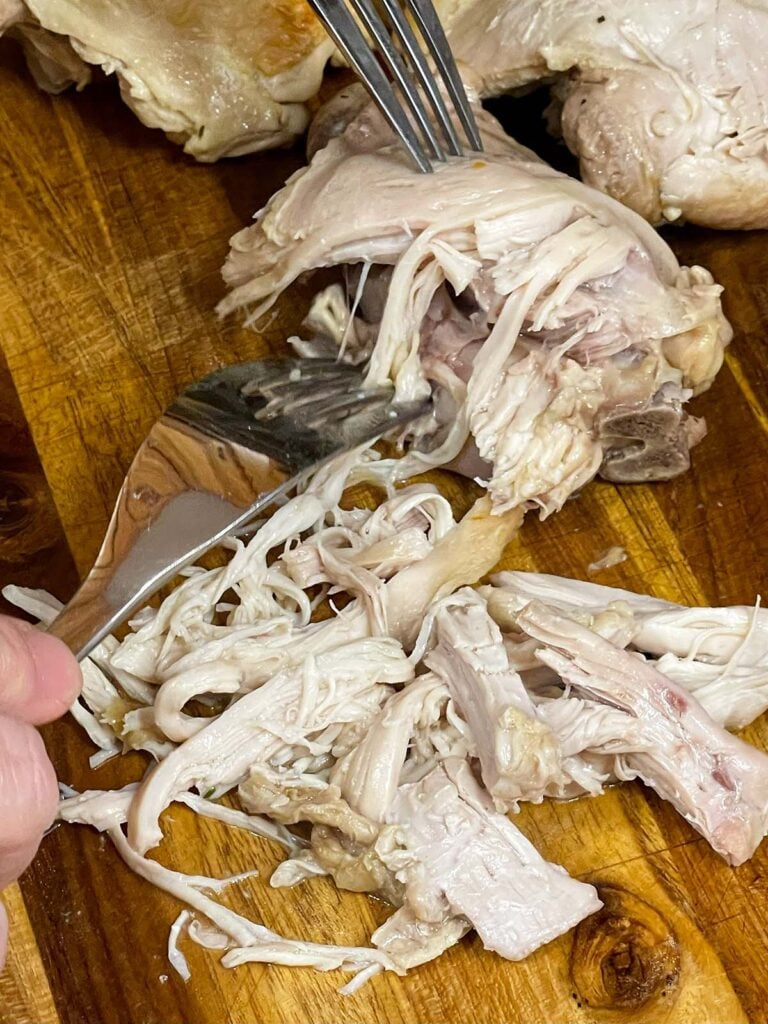 Chicken thigh meat being shredded on a wooden board.