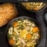 Chicken noodle soup in a dark bowl on a dark surface.