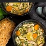 Chicken noodle soup in a dark bowls on a dark surface.