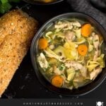 Chicken noodle soup in a dark bowl on a dark surface.