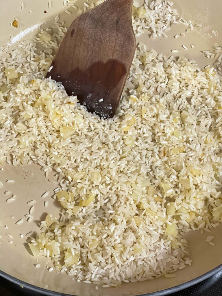 Rice and diced onions sautéing in a cast iron skillet.
