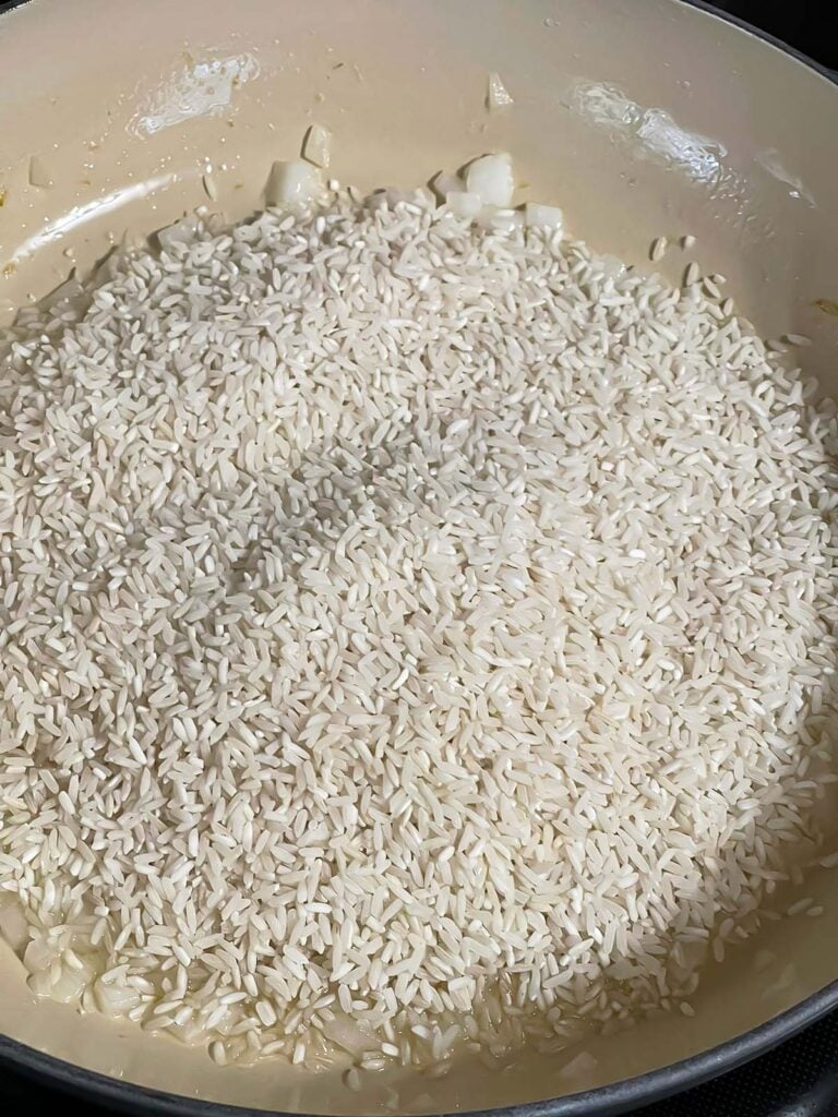 Rice being added to onions cooking in a skillet.