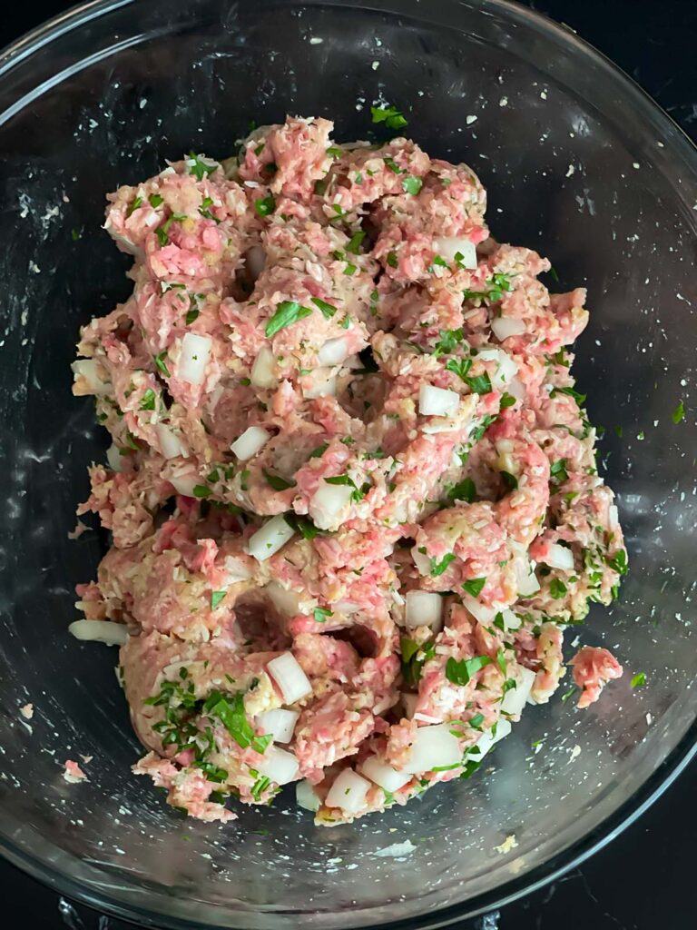 Parmesan meatball mixture in a glass bowl on a dark surface.