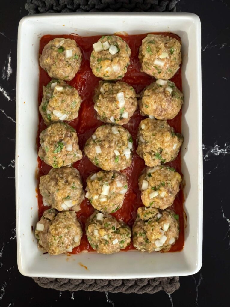 Marinara sauce in the bottom of the casserole dish with the parmesan meatballs placed on top.