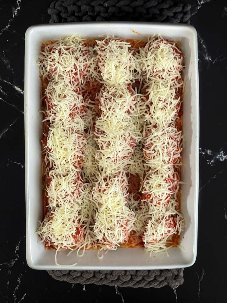 Marinara sauce and shredded Italian blend cheese over the top of the meatballs in a light casserole dish.