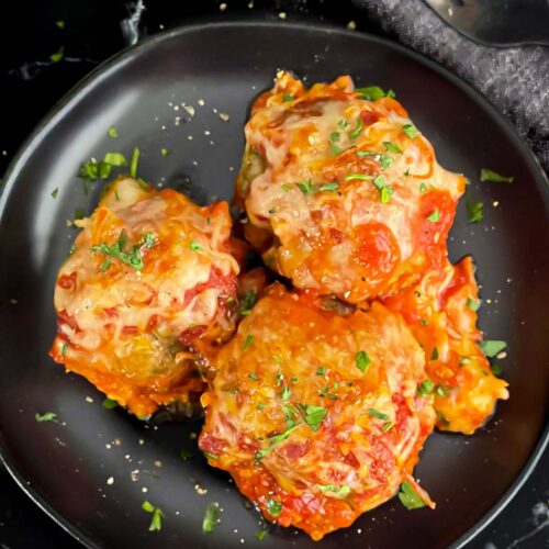 Easy baked parmesan meatballs garnished with chopped Italian flat leaf parsley on a dark plate.