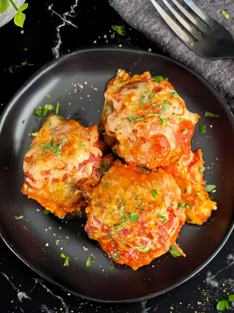 Easy baked parmesan meatballs garnished with chopped Italian flat leaf parsley on a dark plate.