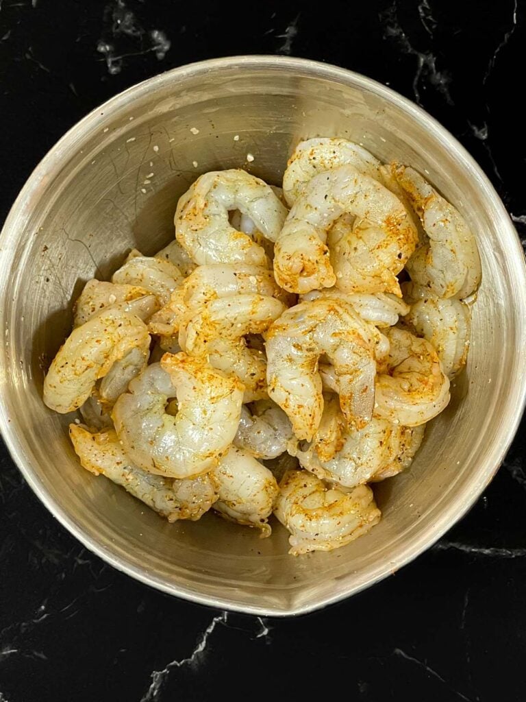 Raw shrimp tossed in seasoning in a stainless steel bowl.