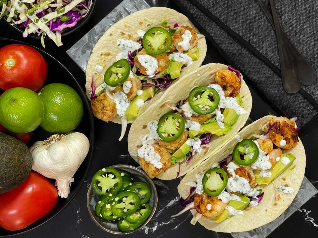 Shrimp tacos served with slaw, jalapeños, and fresh vegetables arranged for a taco-night spread.