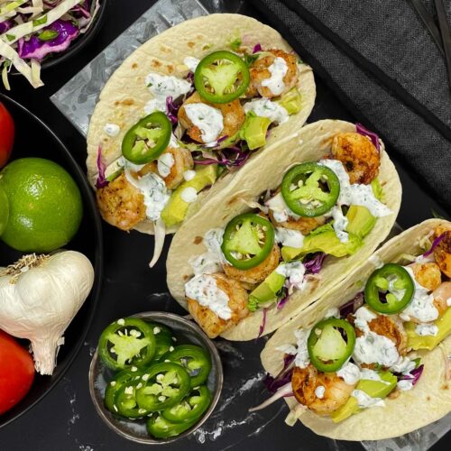 Shrimp tacos served with slaw, jalapeños, and fresh vegetables arranged for a taco-night spread.