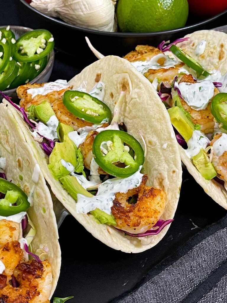 Shrimp tacos served with slaw, jalapeños, and fresh vegetables arranged for a taco-night spread.