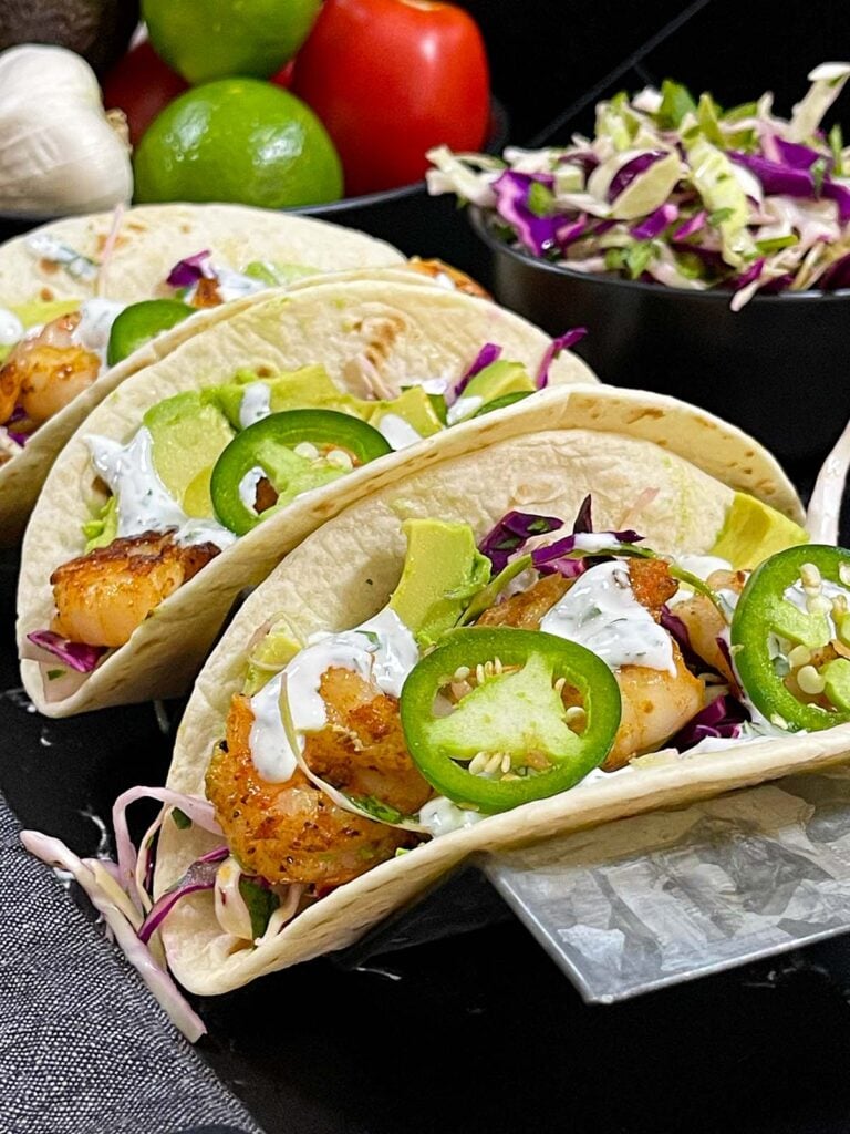 Shrimp tacos served with slaw, jalapeños, and fresh vegetables arranged for a taco-night spread.
