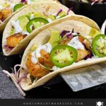 Shrimp tacos served with slaw, jalapeños, and fresh vegetables arranged for a taco-night spread.