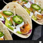 Shrimp tacos served with slaw, jalapeños, and fresh vegetables arranged for a taco-night spread.