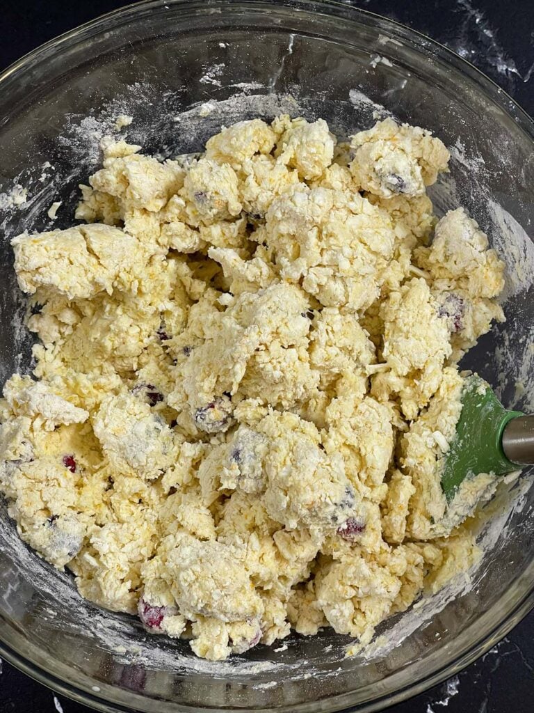 Cranberry orange scone dough in a glass mixing bowl on a dark surface.