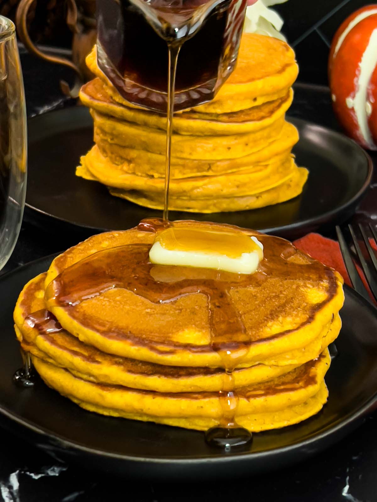 Stack of pumpkin pancakes topped with a pat of butter and syrup on a dark plate.