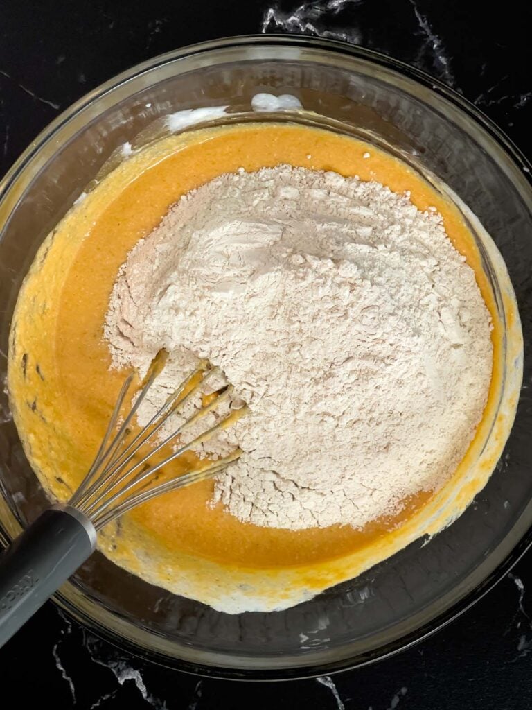 Dry ingredients added to the wet ingredients in a glass bowl for pumpkin pancakes.