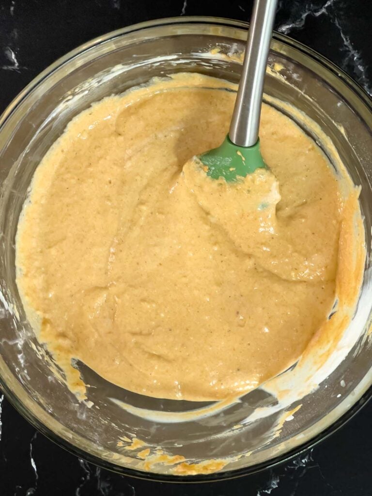 Pumpkin pancake batter mixed in a glass bowl on a dark surface.