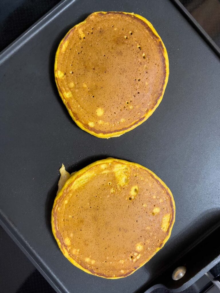 Pumpkin pancakes cooking on a griddle.