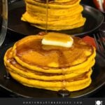 Stack of fluffy pumpkin pancakes with butter and maple syrup, golden edges on a dark plate.