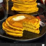 Stack of fluffy pumpkin pancakes with butter and maple syrup, golden edges on a dark plate.