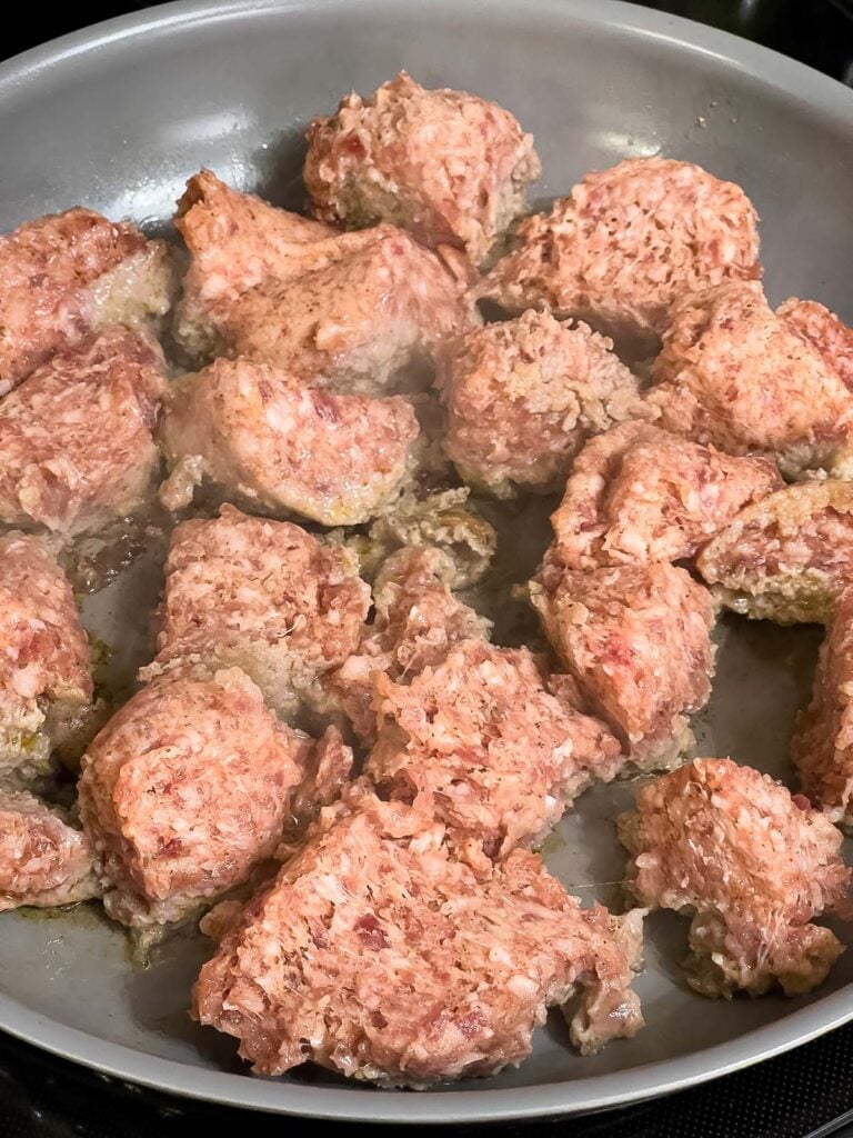 Breakfast sausage browning in large chunks in a skillet.