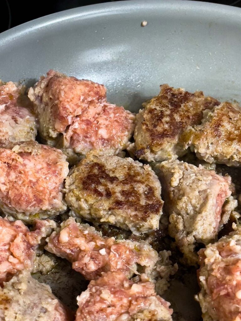 Partially cooked sausage pieces turned to show golden brown searing in a skillet.