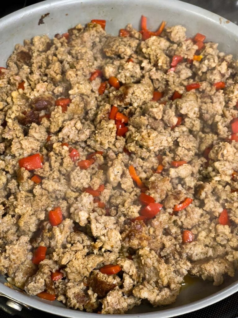 Cooked sausage and softened red bell peppers in skillet.