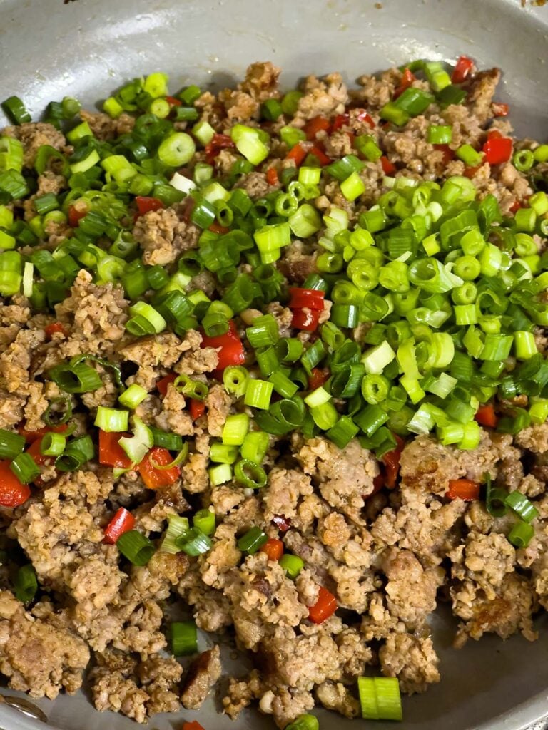 Chopped green onions added to cooked sausage and peppers in skillet.