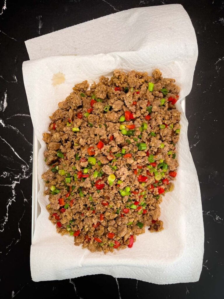Cooked sausage mixture draining on a paper towel-lined plate.