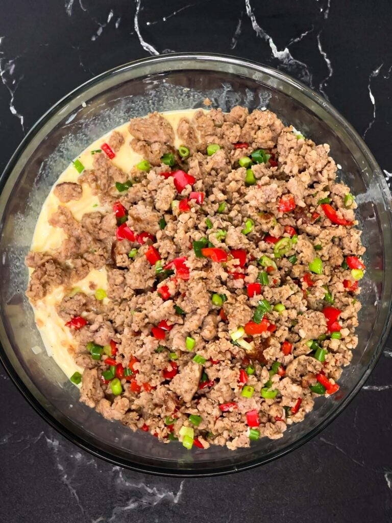 Cooked sausage mixture added on top of egg and hash brown mixture in a bowl.