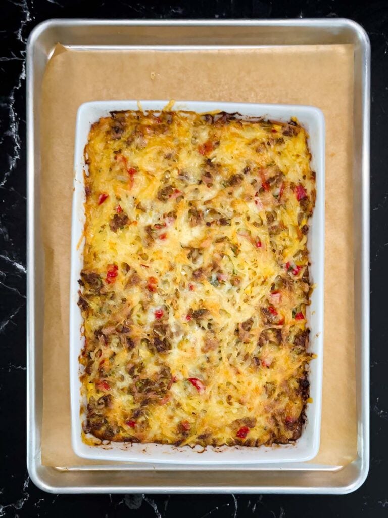 Golden brown baked sausage hashbrown breakfast casserole in 9x13 dish on baking sheet