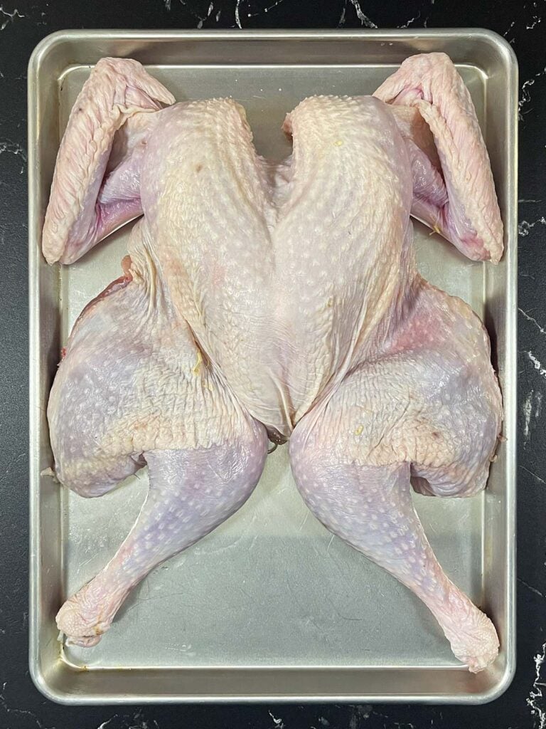 Spatchcocked turkey laid flat on a baking sheet with the backbone removed.