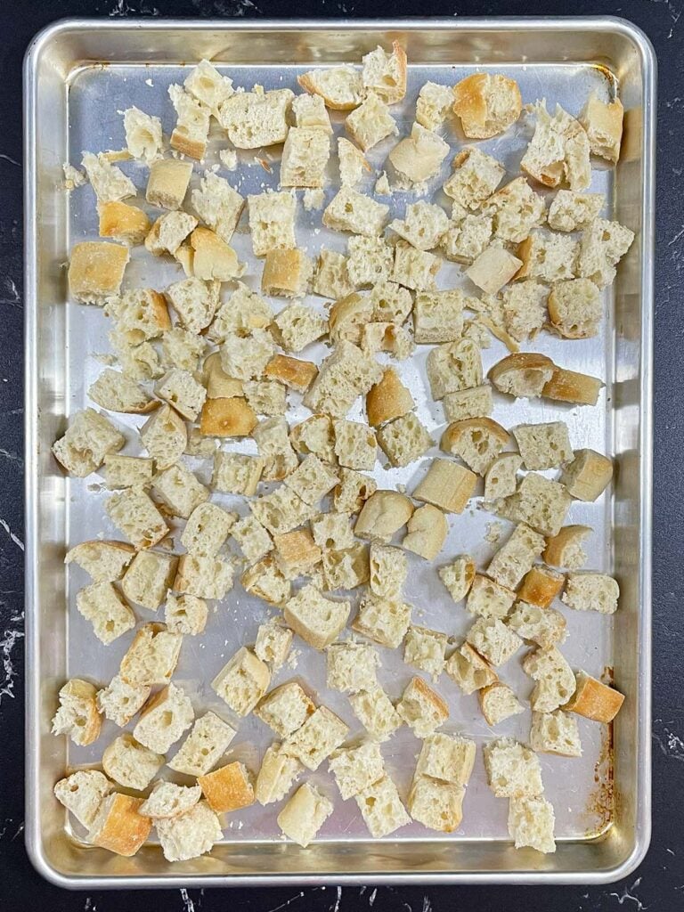 Cubed ciabatta bread spread on a baking sheet for drying.