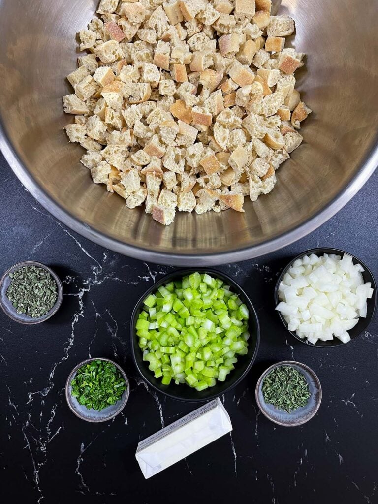 Dried bread cubes in a large bowl with celery, onion, and herbs prepared for stuffing.