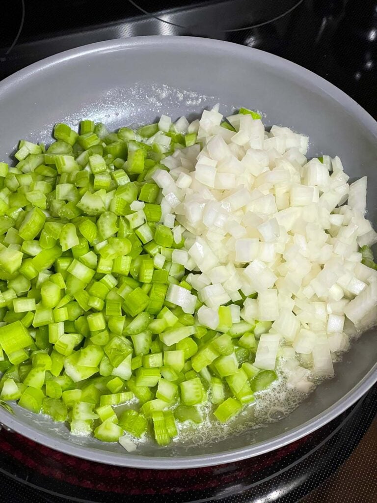 Diced onion and celery cooking in butter in a skillet.