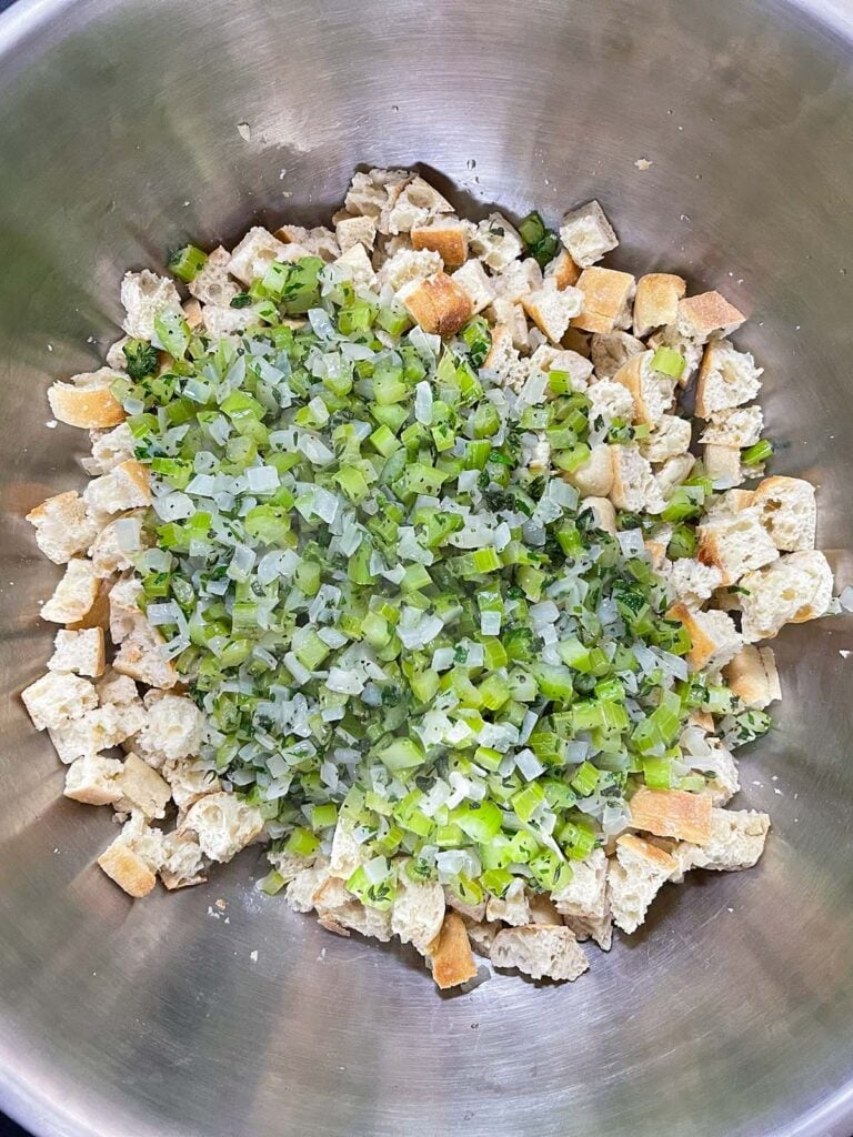 Cooked vegetables added to dried bread cubes in a mixing bowl before combining.
