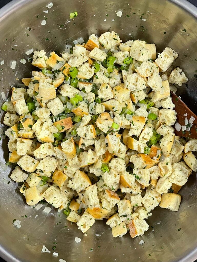Stuffing mixture of bread, vegetables, and herbs fully combined in a bowl.