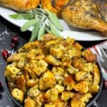 A bowl of stuffing in a dark bowl with a spatchcocked turkey in the background.