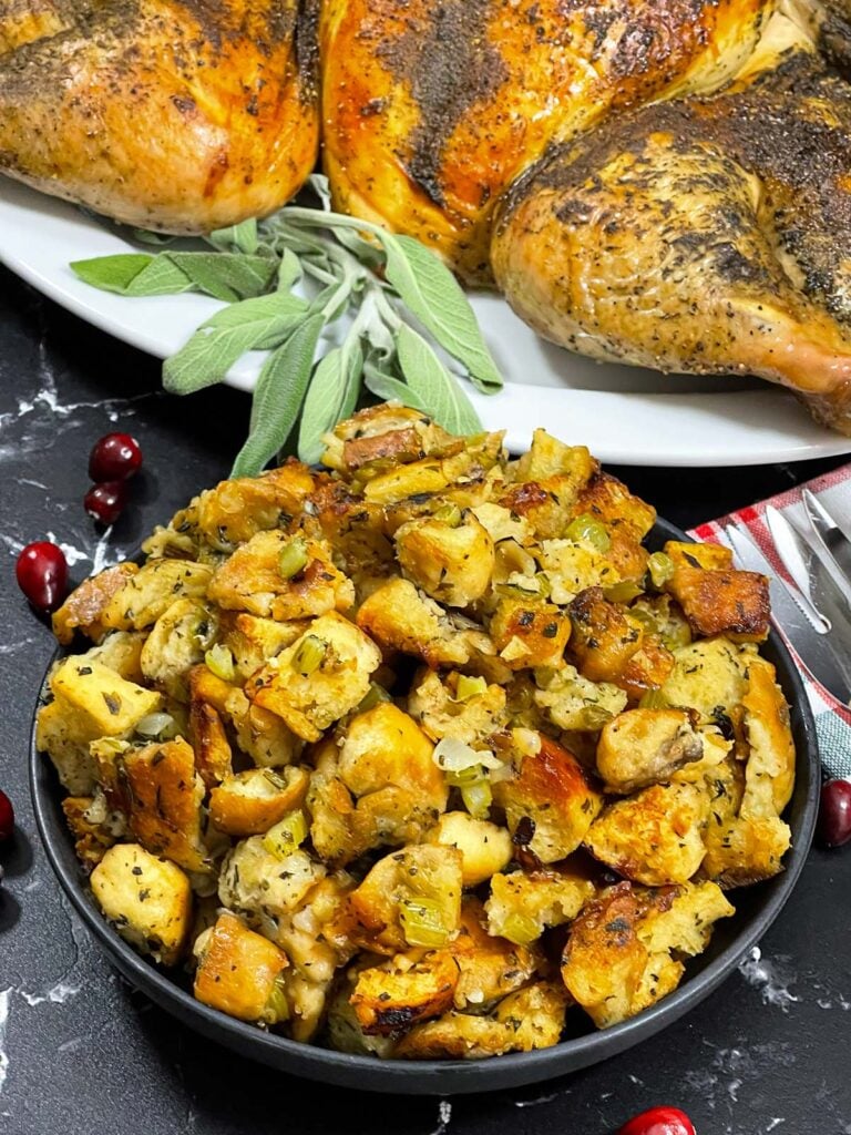 A bowl of stuffing in a dark bowl with a spatchcocked turkey in the background.