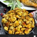 A bowl of stuffing in a dark bowl with a spatchcocked turkey in the background.